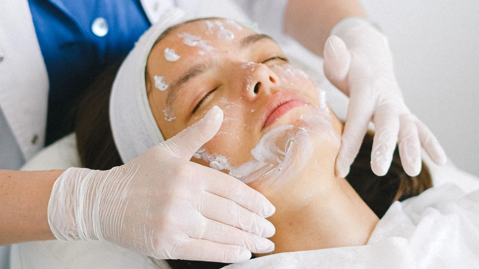 Esthéticienne réalisant un soin du visage à une cliente allongée en cabine épurée