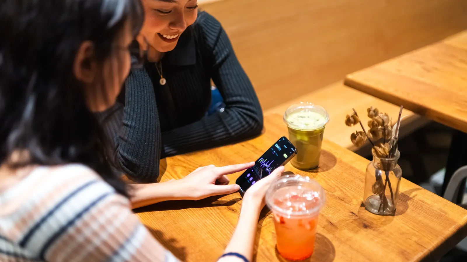 Deux clientes attablées dans un café regardent un smartphone