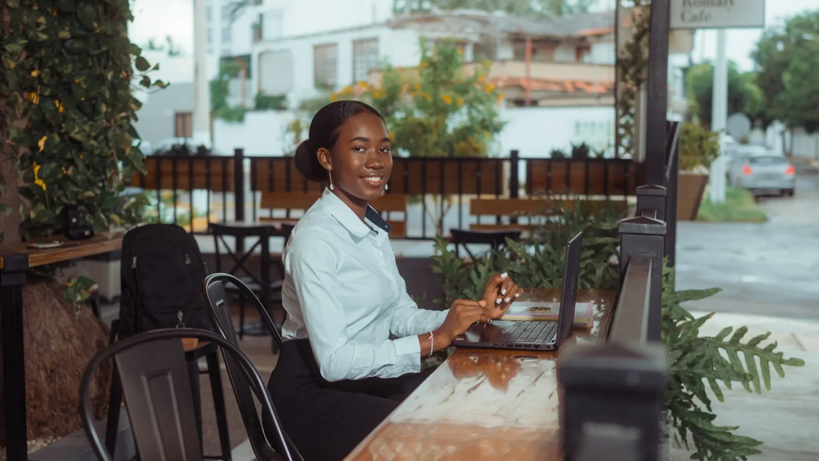 Commerçante souriante gérant son activité sur un ordinateur portable en terrasse