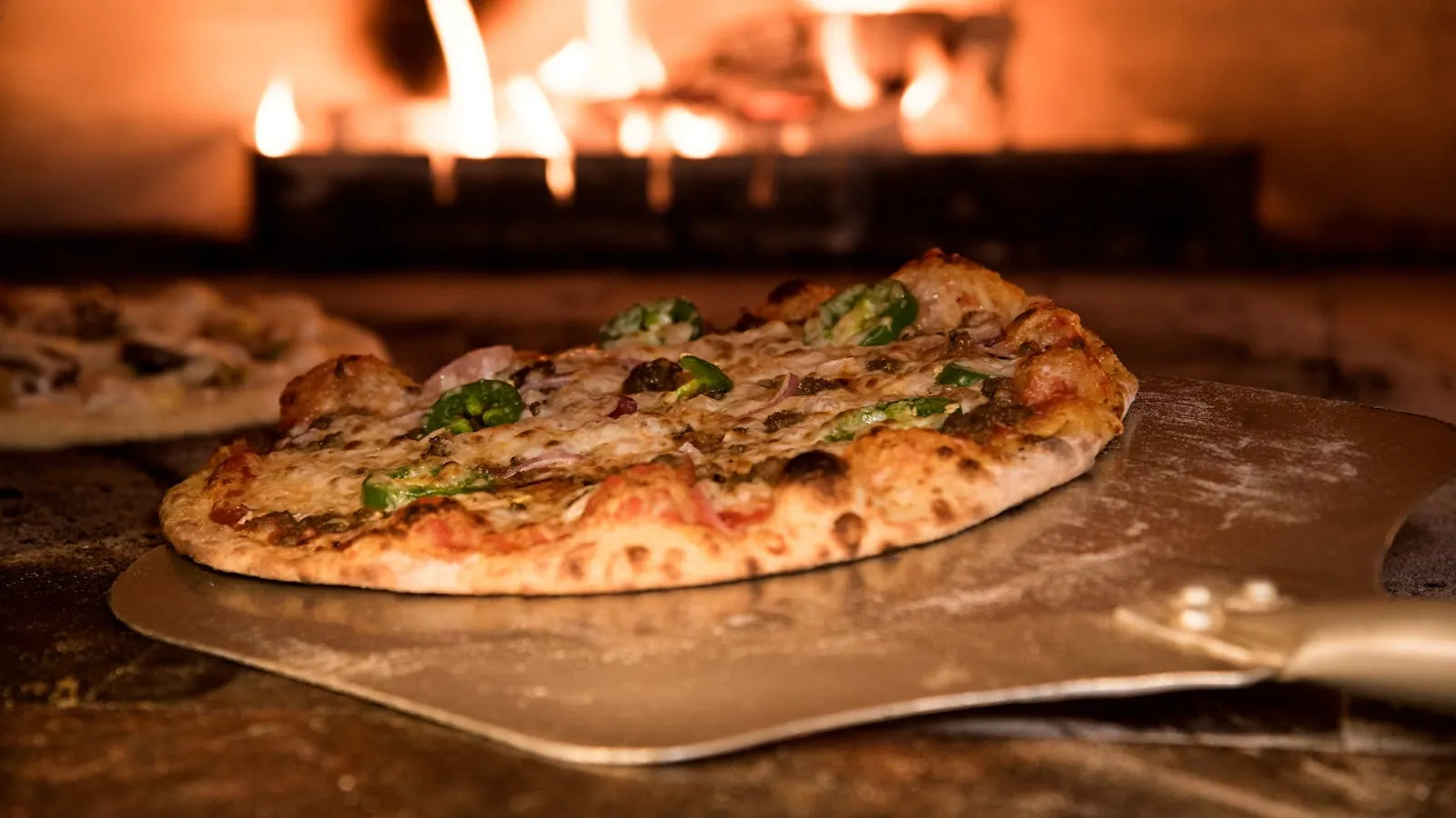 Pizzaïolo enfournant une pizza au feu de bois dans une pizzeria artisanale