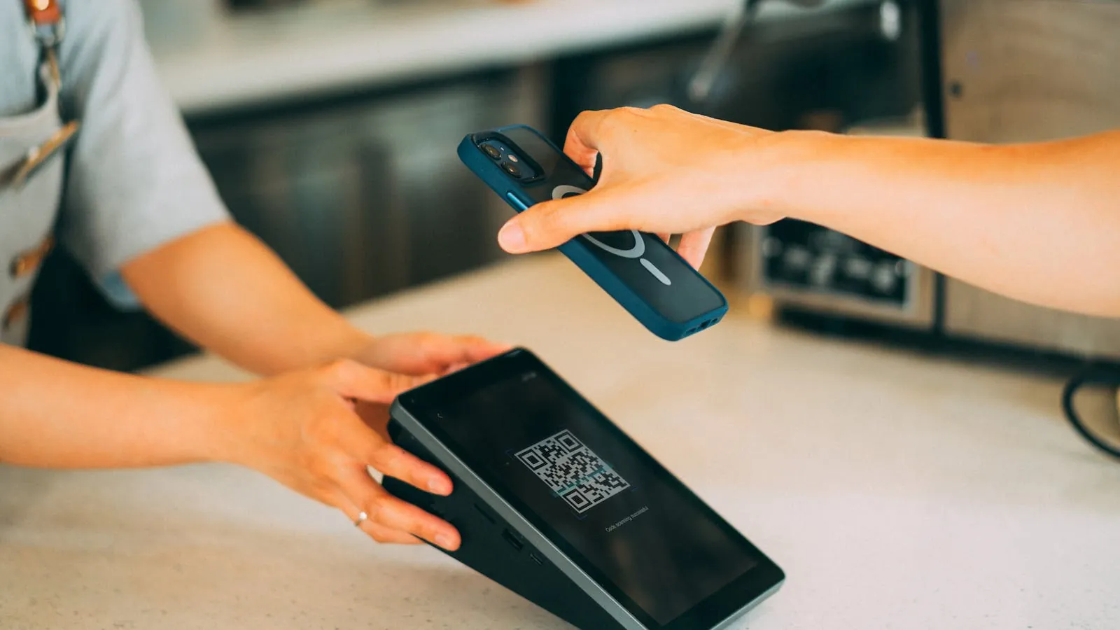 Main qui scanne avec un smartphone un QR code posé sur le comptoir d'une boutique au moment du paiement